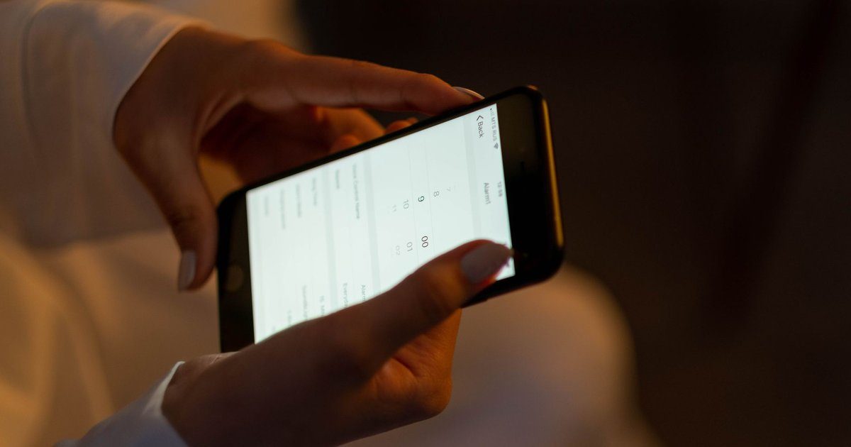 Two hands hold a smartphone with an app open, the way a caregiver checks in and out of a visit with an EVV app.