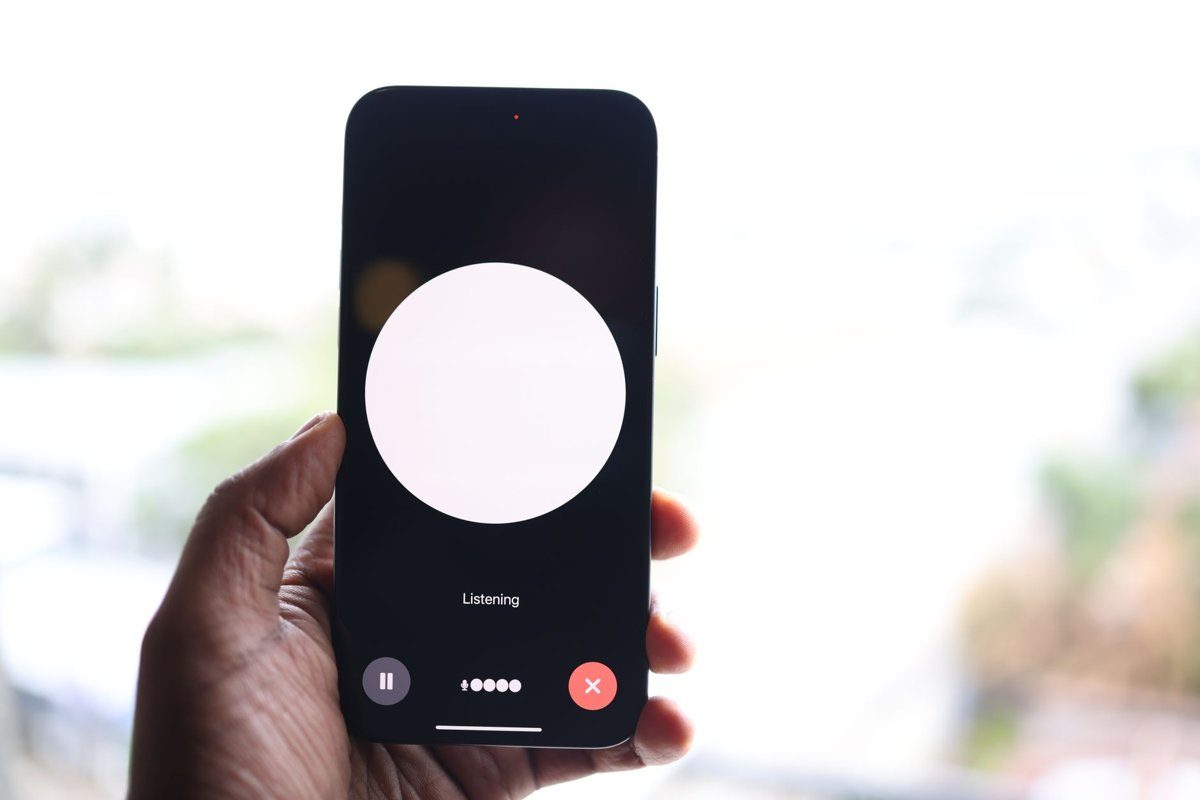 A hand holds a smartphone showing a voice assistant screen with the word Listening under a large white circle.